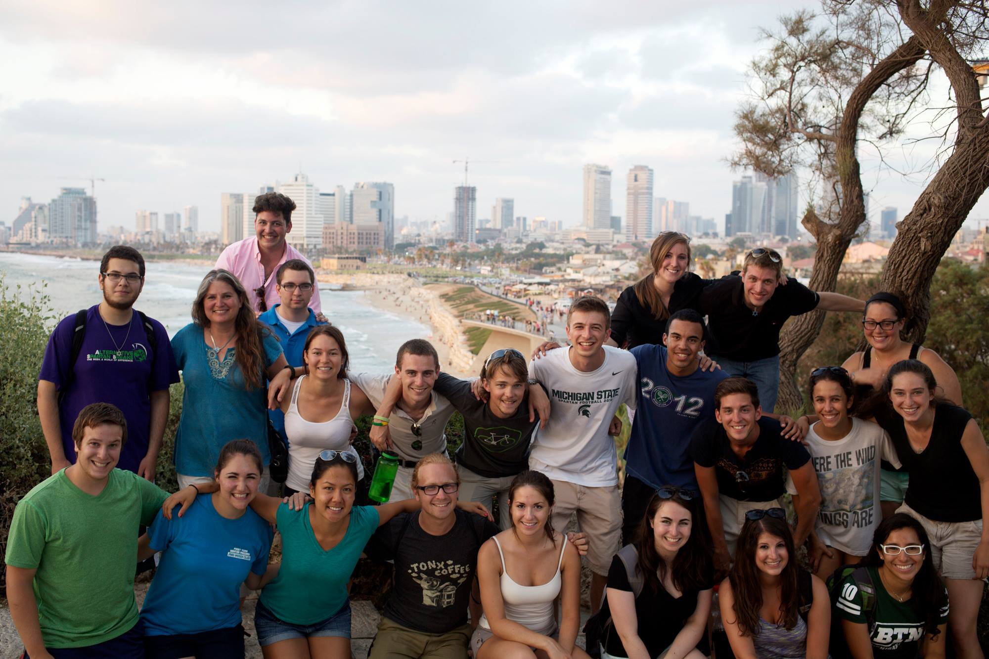 A diverse group of college students stand for a photo opportunity in Israel, the desert behind them.