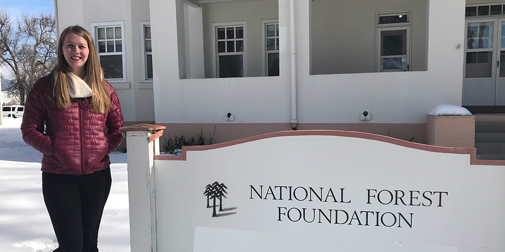 Hannah Ettema stands in front of a sign reading "National Forest Foundation" on a snowy day