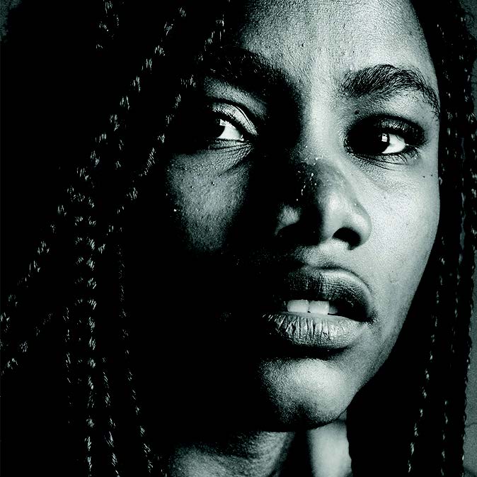 A black and white closeup photo of a Afro-descendant, Black Puerto Rican, and Caribbean woman with long braids, looking at the camera