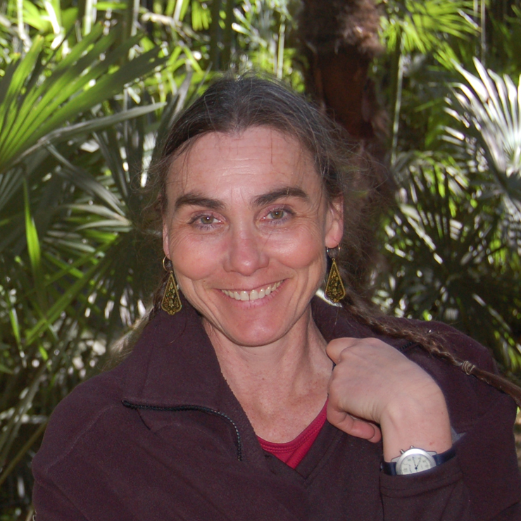 A white woman with a wide smile and graying hair, wearing a dark brown fleece jacket and dangling gold earrings