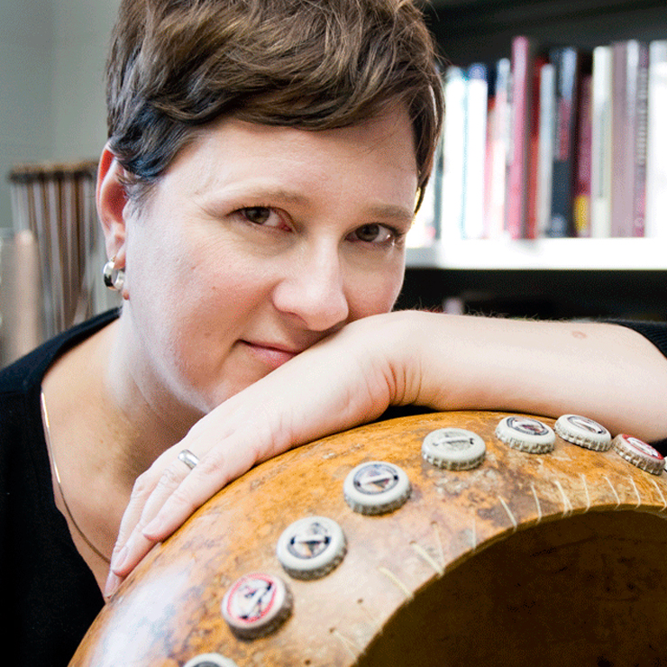 A white woman with short brown hair leans on a large drum.