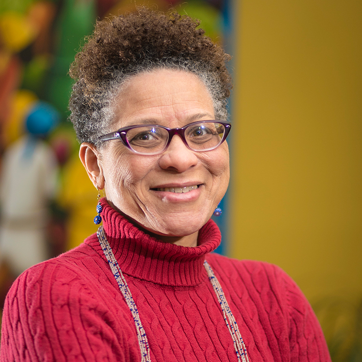 A Black woman smiling at the camera, wearing a bright red sweater, earrings, and dark glasses.