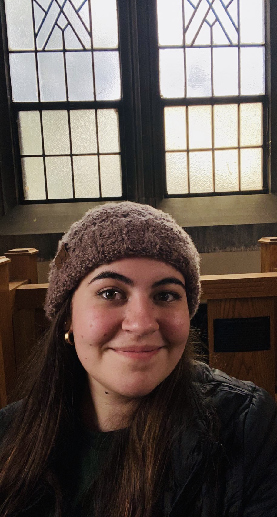 Image shows a young woman with a brown hat smiling in front of old windows