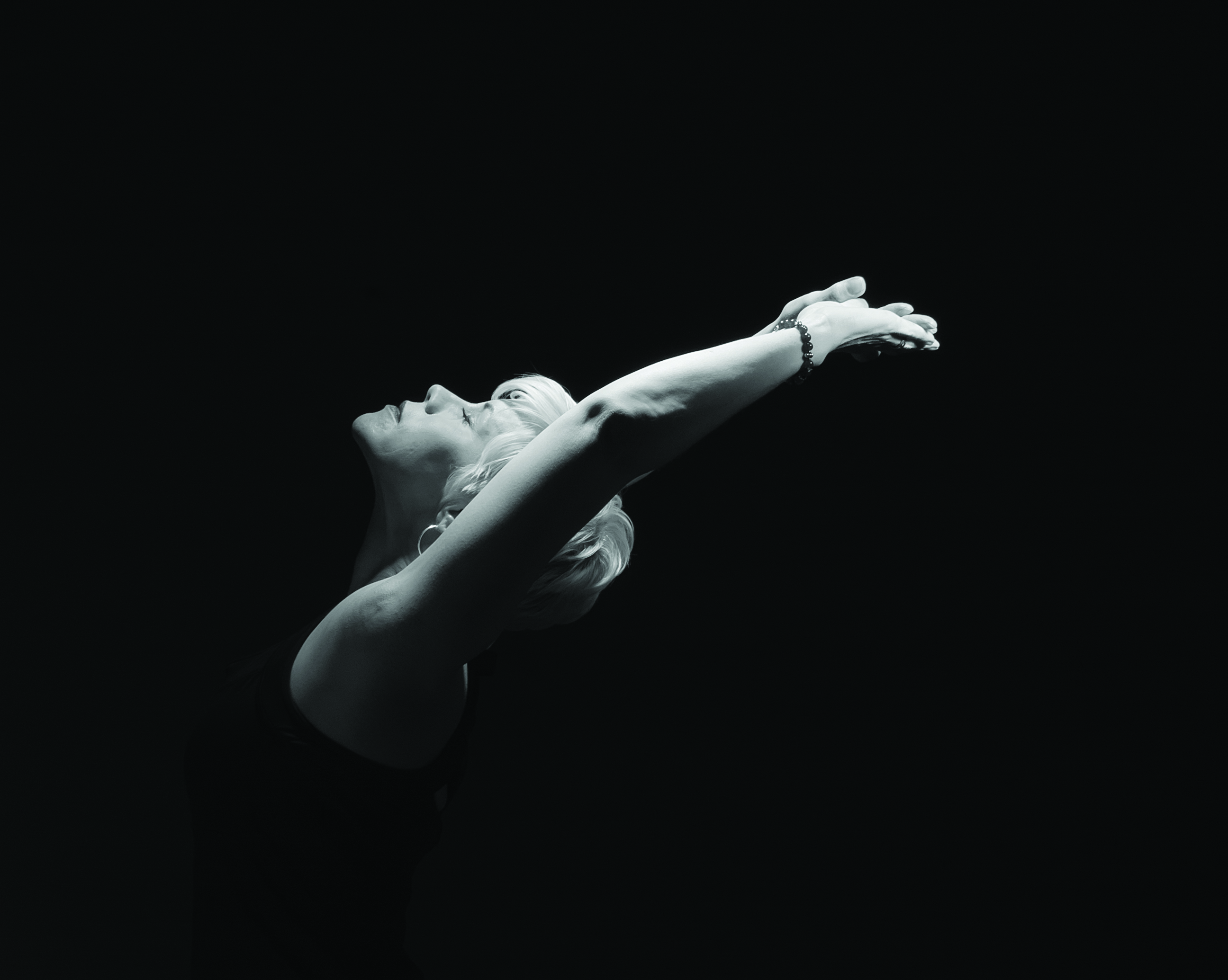 A black and white picture featuring a white woman doing yoga, reaching upwards.