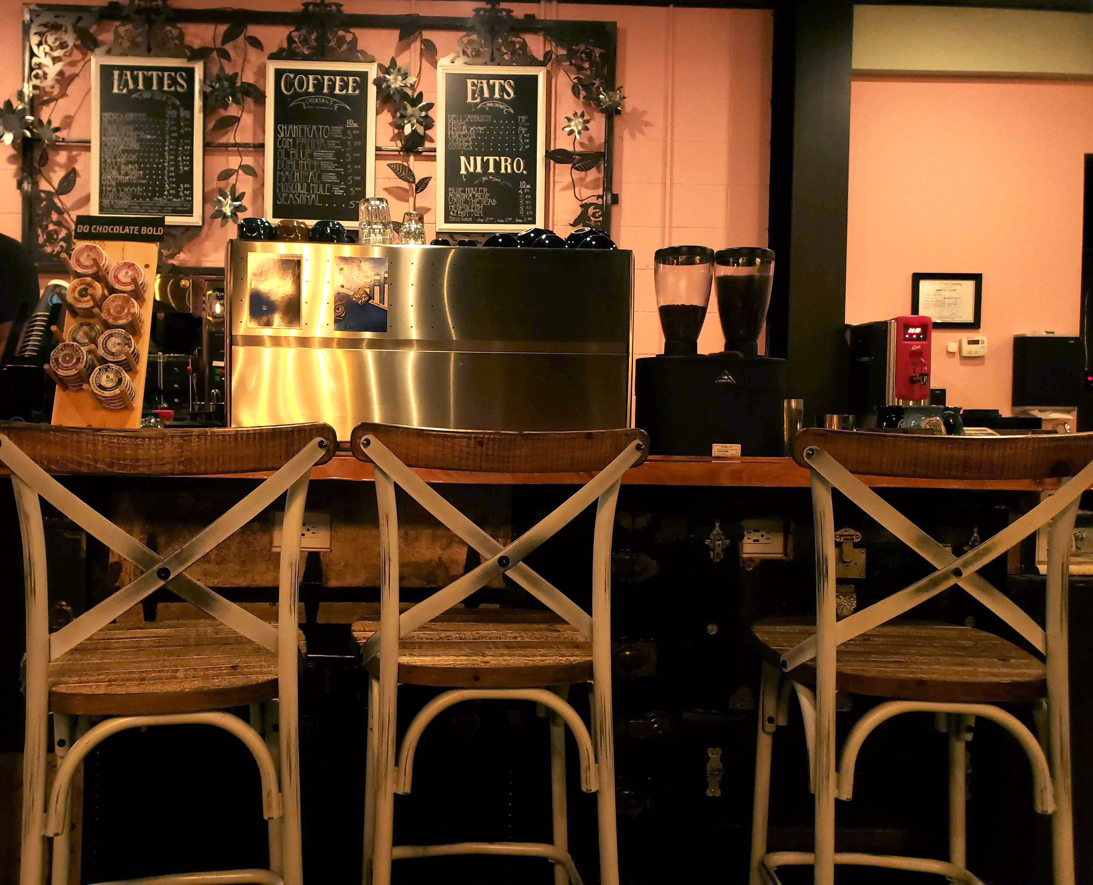 Image shows three small blackboards bearing handwritten titles of beverages on a pale pink wall.