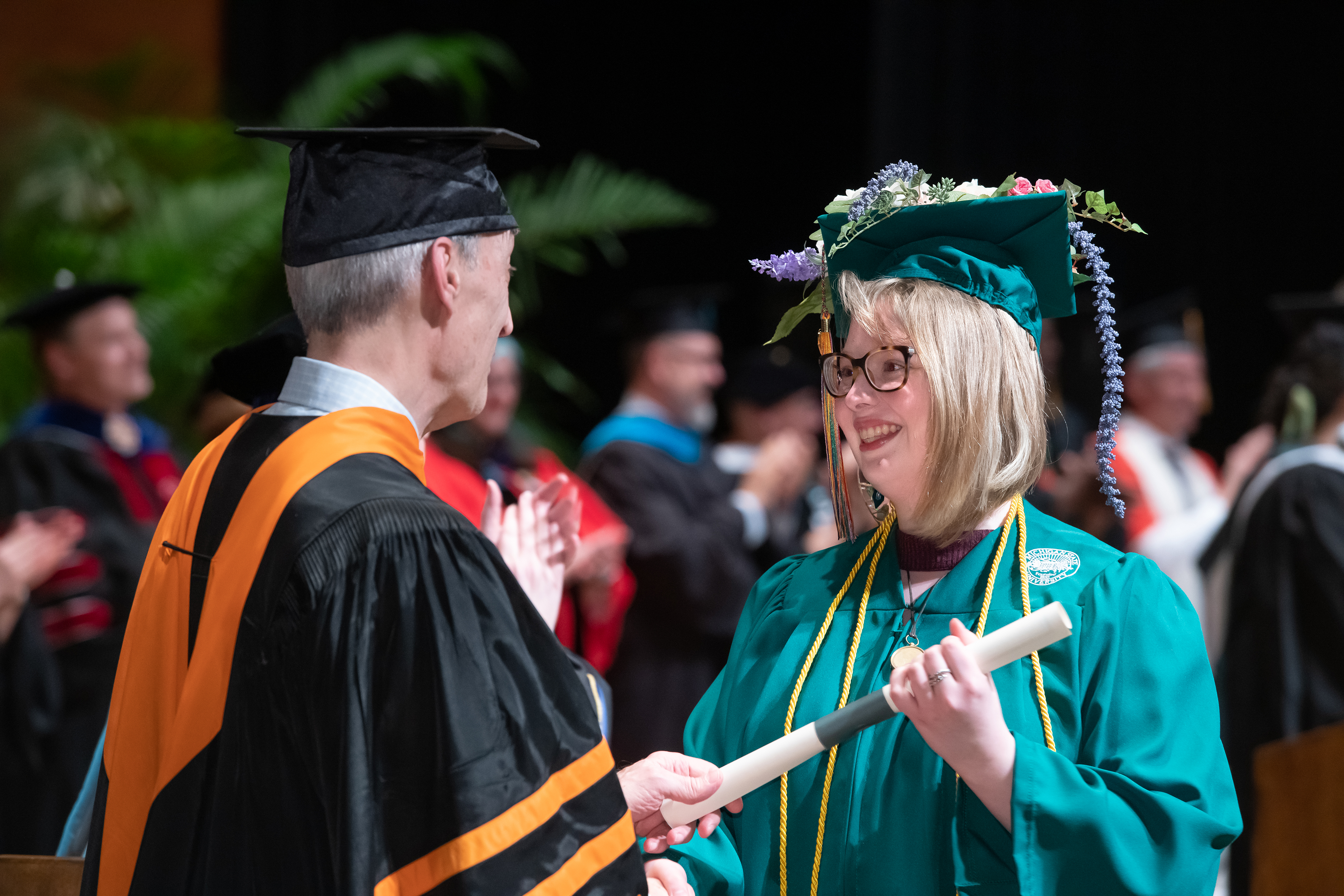 Dean Steve, an older white man in regalia, congratulates a white female student in green graduation robes.
