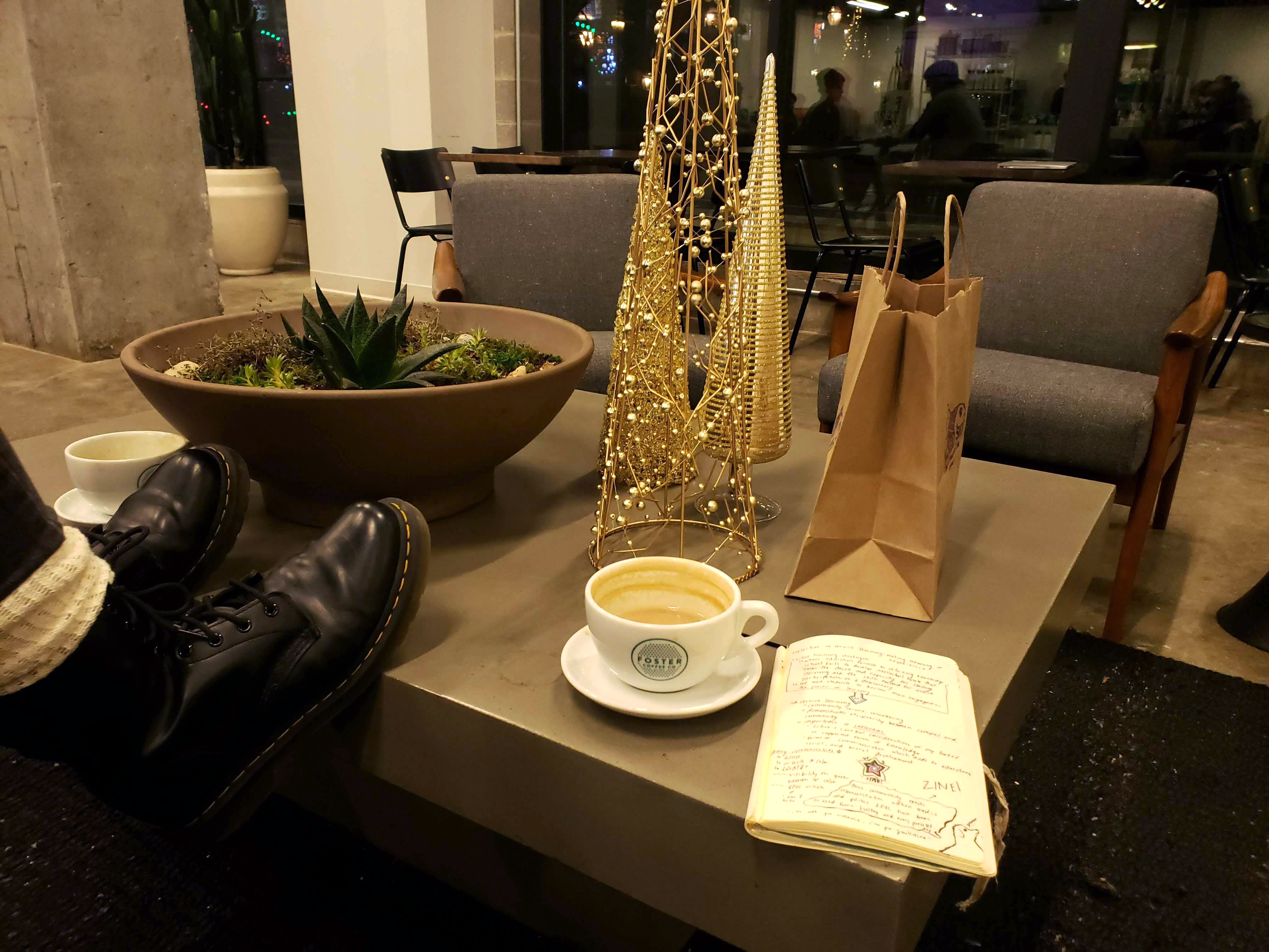 Image shows a coffee table with someone's feet on the table, relaxing next to a branded Fosters cup of coffee and seasonal decor.