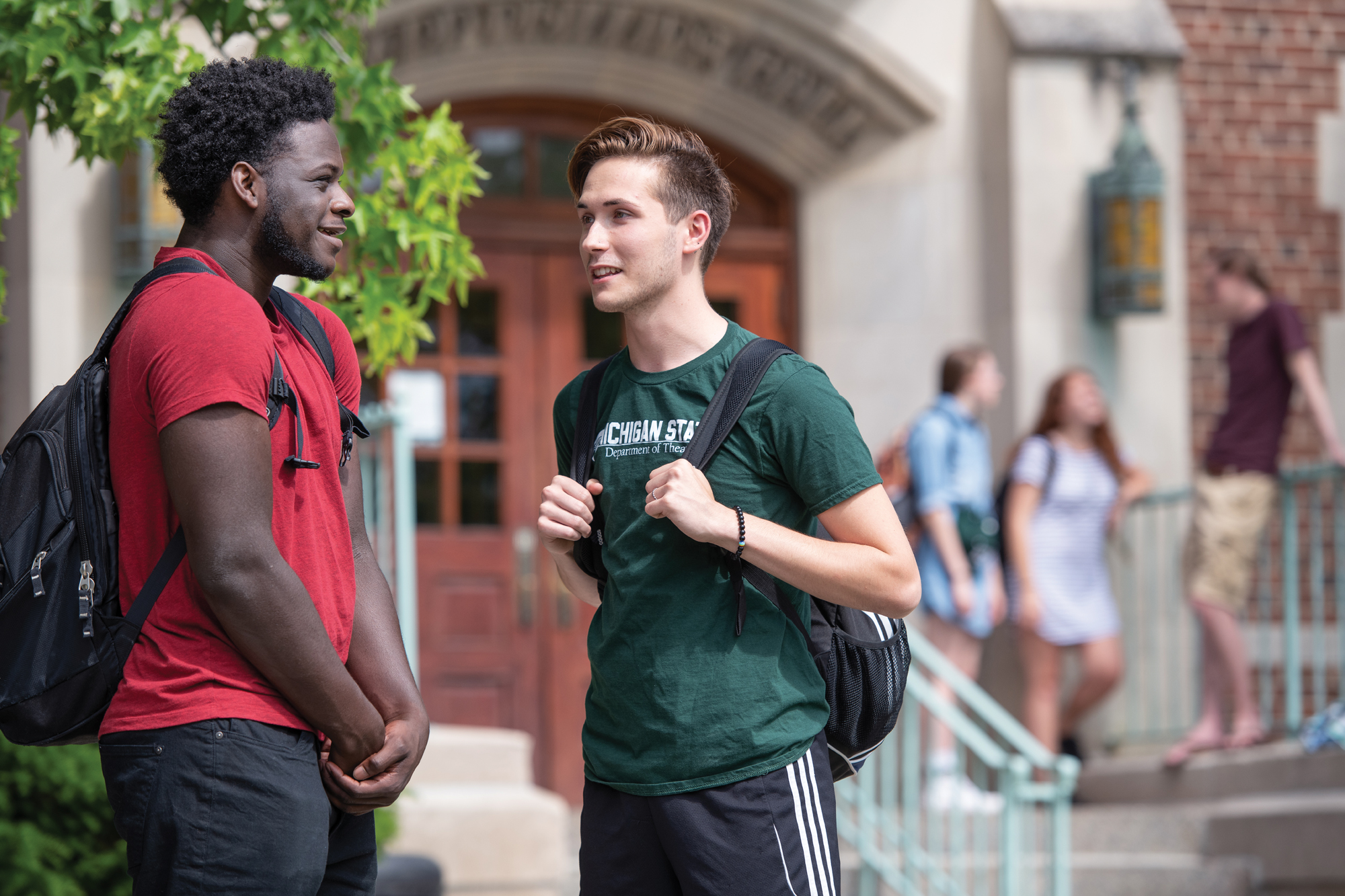 An African American and a White student converse outside of a brick building, Phillips Hall.
