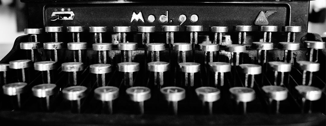 Image shows a black and white photo of an old typewriter, with a close-up on the keys.