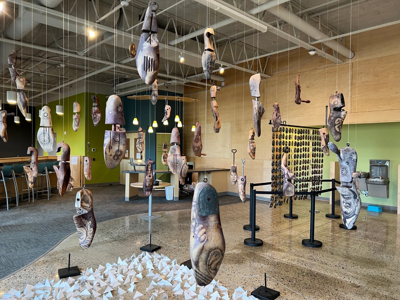 Image shows art installation by artist Mo Juaw: wooden shoe forms suspended from ceiling with various illustrations on them