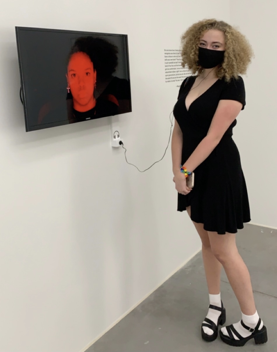 RCAH student Maggie Lupton in front of her film "Civil Trinity" at the Broad, with a still of RCAH Student Vanessa Thompson on the TV screen