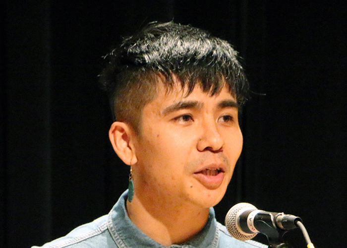 A young Vietnamese man, Ocean Vuong, stands on stage reading.