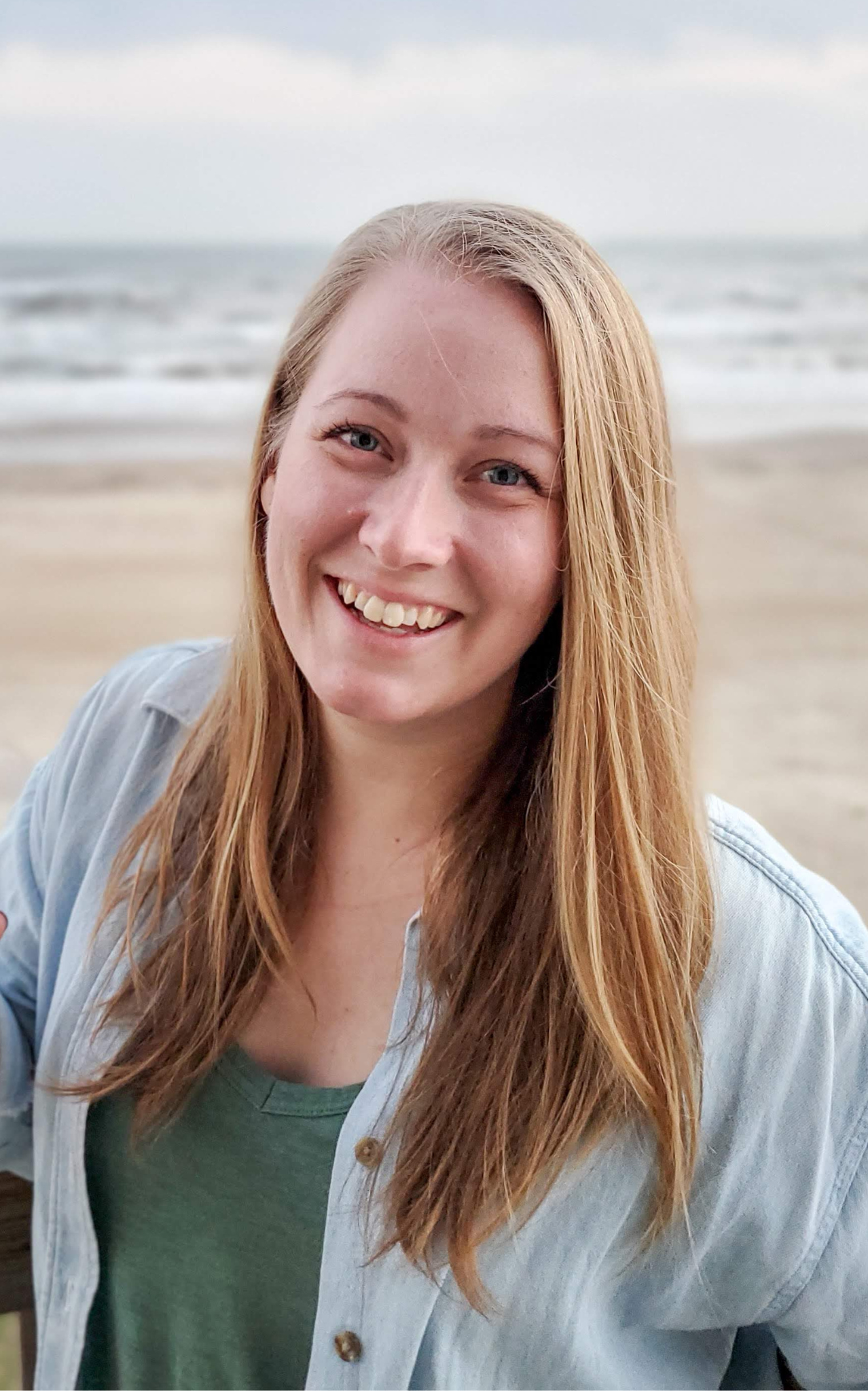 Image shows a young blonde woman with long, straight hair wearing a jean jacket and smiling at the camera